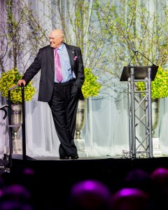 man on stage at an event leaning and smiling off camera, professional portraits