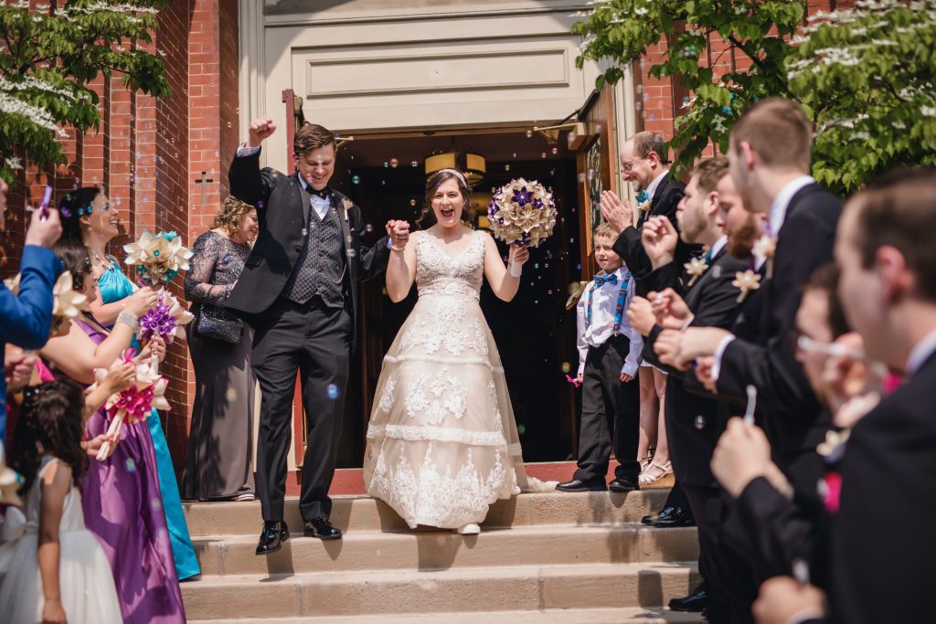 the stone couple cheering and coming out of the church doors to a crowd and bubbles. Photo captured by Dave Zerbe Photography